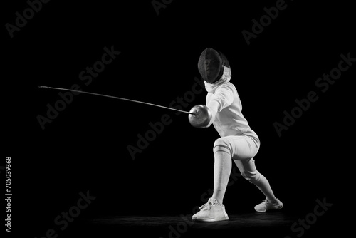Fencer lunges forward, her blade in motion against black studio background. She is focused and determined, swordswoman prepare to clash. Concept of professional sport, active lifestyle, championship.