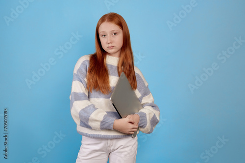 Confident redhead teenage girl holding laptop on blue background in studio. © Ирина Щукина