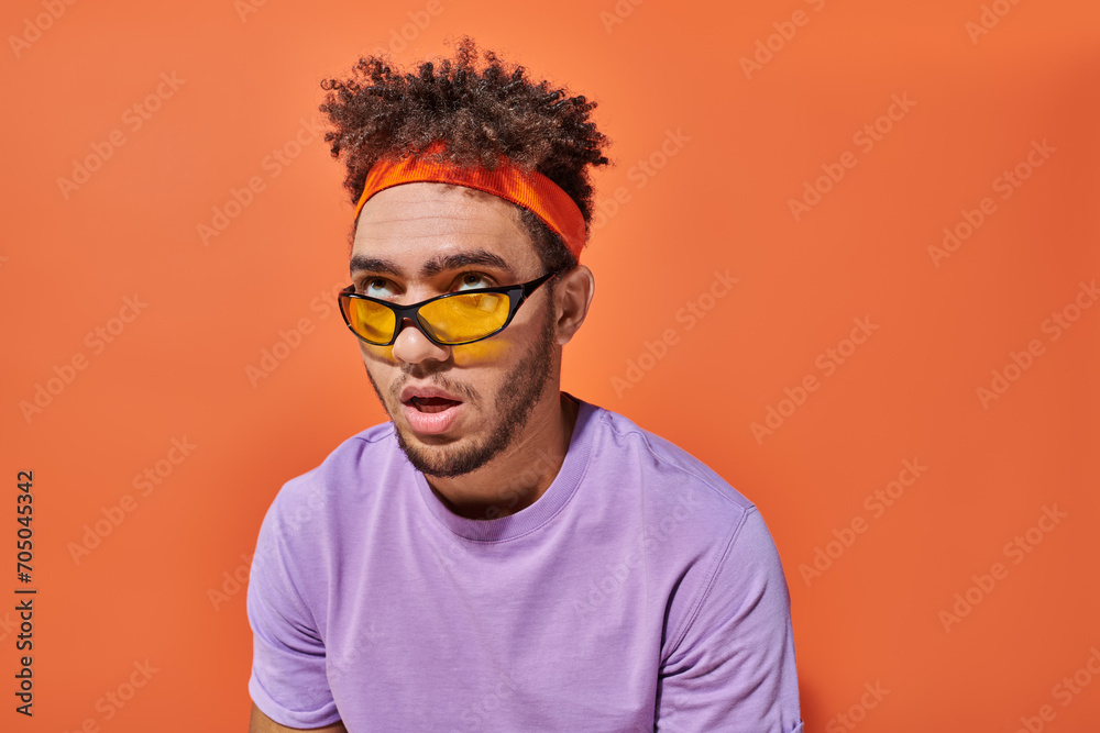 annoyed african american man in eyeglasses and headband rolling eyes on orange background