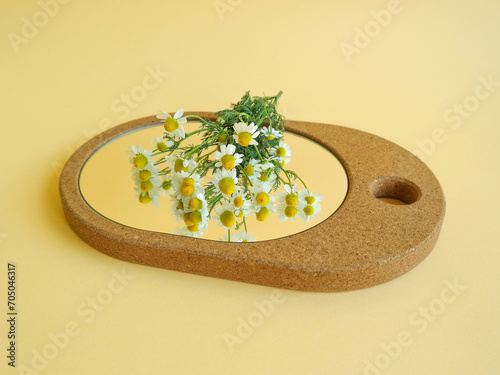 Creative layout made of elegant cork mirror and chamomile flowers against pastel yellow background. Natural minimal concept. Flower reflection. Copy space.