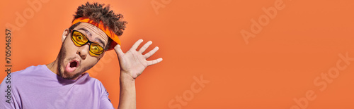 banner, african american man with surprised face expression adjusting headband on orange background photo