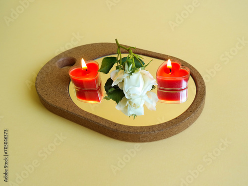 Creative floral layout made of elegant mirror, white rose and two red heart shaped candles against gradient yellow background. Natural minimal concept. Flower reflection. Valentine's design. Love.