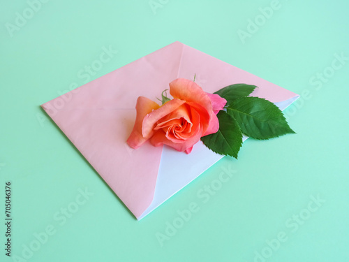 Romantic layout made of pink envelope and gradient pink and orange rose flower against pastel mint green background. Woman's day. Valentine design.
