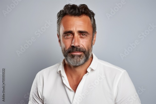 Portrait of a handsome mature man in a white shirt looking at the camera while standing against grey background