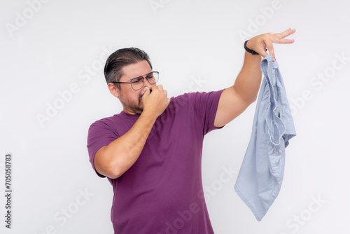 A disgusted middle aged man covers his nose while holding a stinky and smelly pair of boxer shorts with his hand. Isolated on a white background. photo