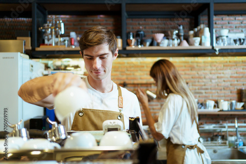 Professional caucasian coffee barista making a cup of coffee by using a modern espresso machine. Barista serving a cup of coffee to female customer over the coffee bar.