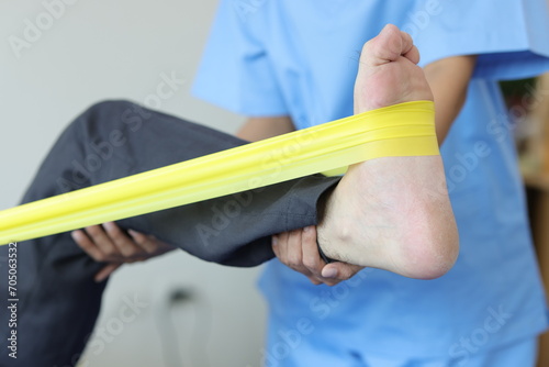Physiotherapist nurse treating patient with exercise using elastic band therapy rehabilitating man leg. Concept of physical therapy and rehabilitation.