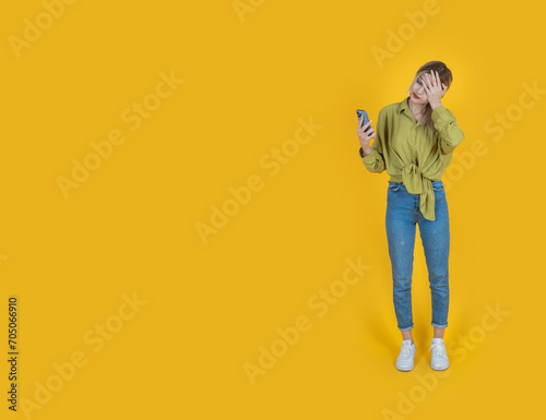 Sad young woman, full body length caucasian sad young woman. Desperately looking smartphone. Waiting good news. Feeling bad. Depressed, anxious student. Isolated yellow, copy space.