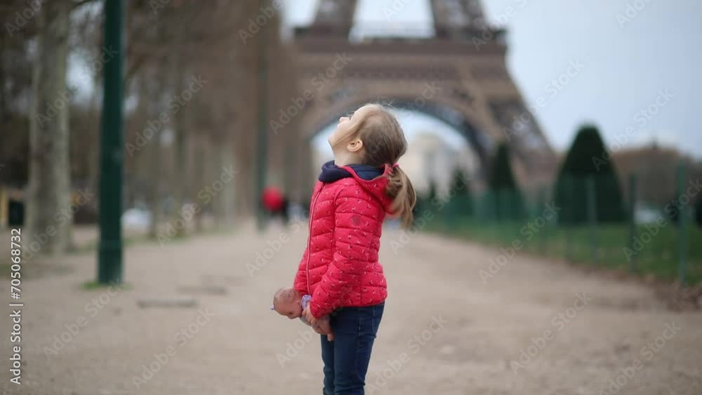 Adorable preschooler girl with a doll in front of the Eiffel tower in Paris, France Adorable preschooler girl with a doll in front of the Eiffel tower in Paris, France