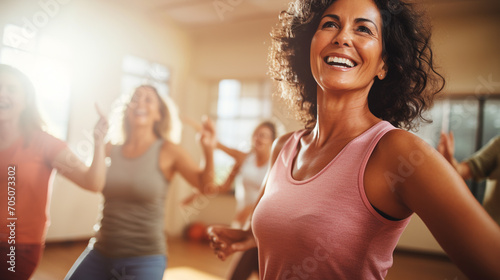 Middle-aged women enjoying a fun class in a dance sports group, expressing their active lifestyle through Zumba, and in front of them all is one woman who smiles genuinely, radiating health