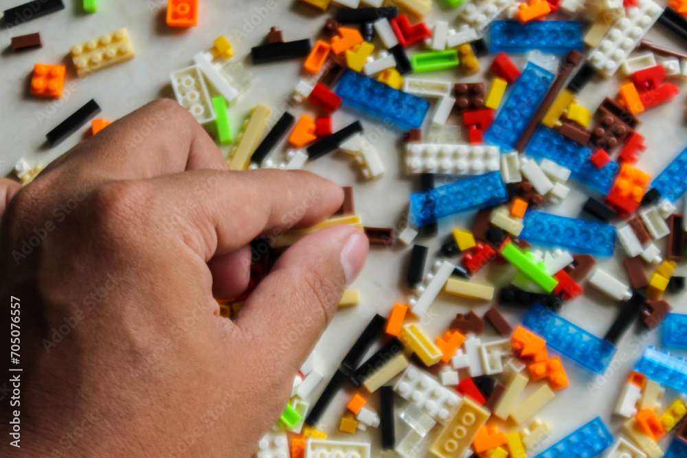 man hand arranging pile of colorful Lego blocks. Top angle view of hand holding lego bricks on white background - obrazy, fototapety, plakaty 