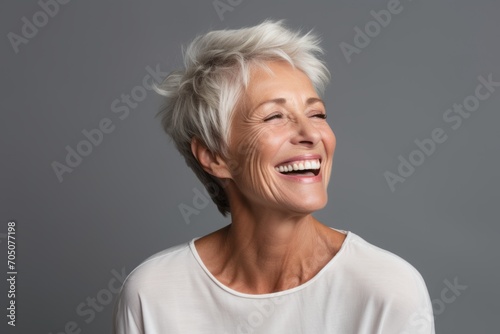 Cheerful mature woman laughing and looking up over grey background.