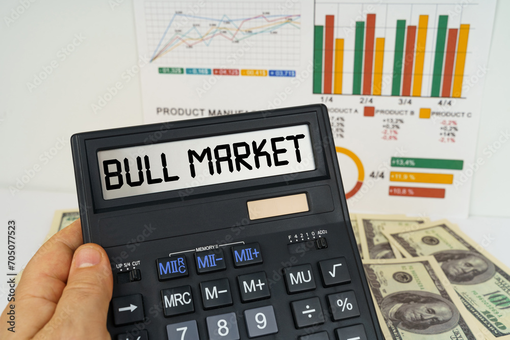 On the table there are financial reports, dollars, in the hands of a calculator with the inscription - bull market On the table there are financial reports, dollars, in the hands of a calculator with the inscription - bull market