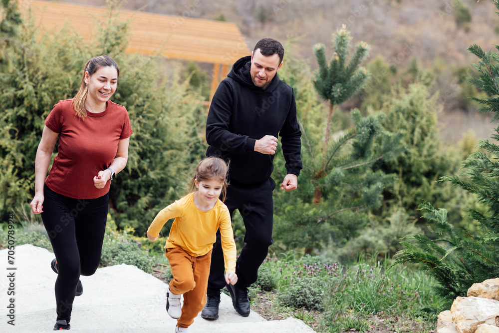 Fototapeta premium Happy family jogging in the summertime. Smiling young couple with their cute daughter doing sport