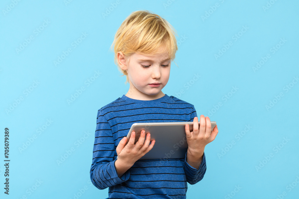 Young child holding digital tablet. Boy watching videos on his computer, isolated over pastel blue background. Children and technology. Young child holding digital tablet. Boy watching videos on his computer, isolated over pastel blue background. Children and technology.