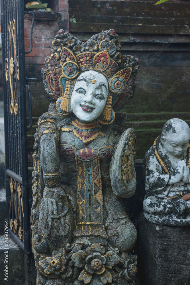 a vertical view of an old stone statue in a garden in the temple of bali