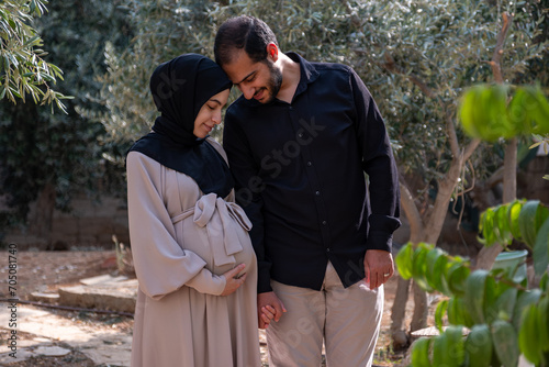 A husband walks with his pregnant wife in the park, exchanging loving glances and feeling excited about the approaching time of birth photo