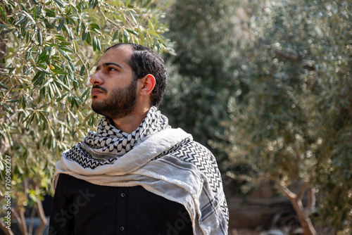 portrait for male wearing keffiyeh in olive tree field with black background and black shirts also with angry facial expression