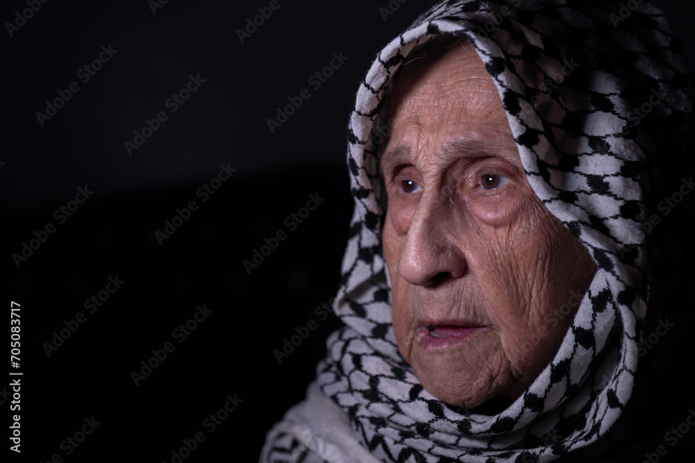 portrait of an old lady in dark background wearing white palestinian keffiyeh with smile on her face looking for freedom and hope to Right of Return for Palestinians