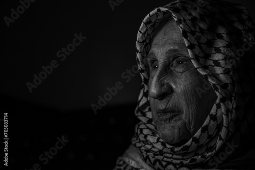 portrait of an old lady in dark background wearing white palestinian keffiyeh with smile on her face looking for freedom and hope to Right of Return for Palestinians photo