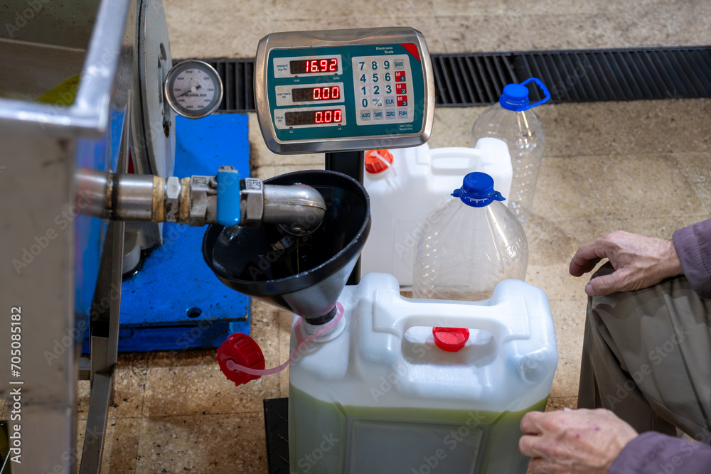 An old Muslim man is filling fresh olive oil into plastic gallons using a funnel and weighing scale in a pressing factory An old Muslim man is filling fresh olive oil into plastic gallons using a funnel and weighing scale in a pressing factory