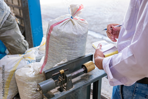 man handsholding pen in front of scale weighing packs ,weighing sacks of olives photo