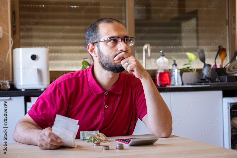 man sitting in the kitchen and calculating the costs of living feeling frustrated man sitting in the kitchen and calculating the costs of living feeling frustrated