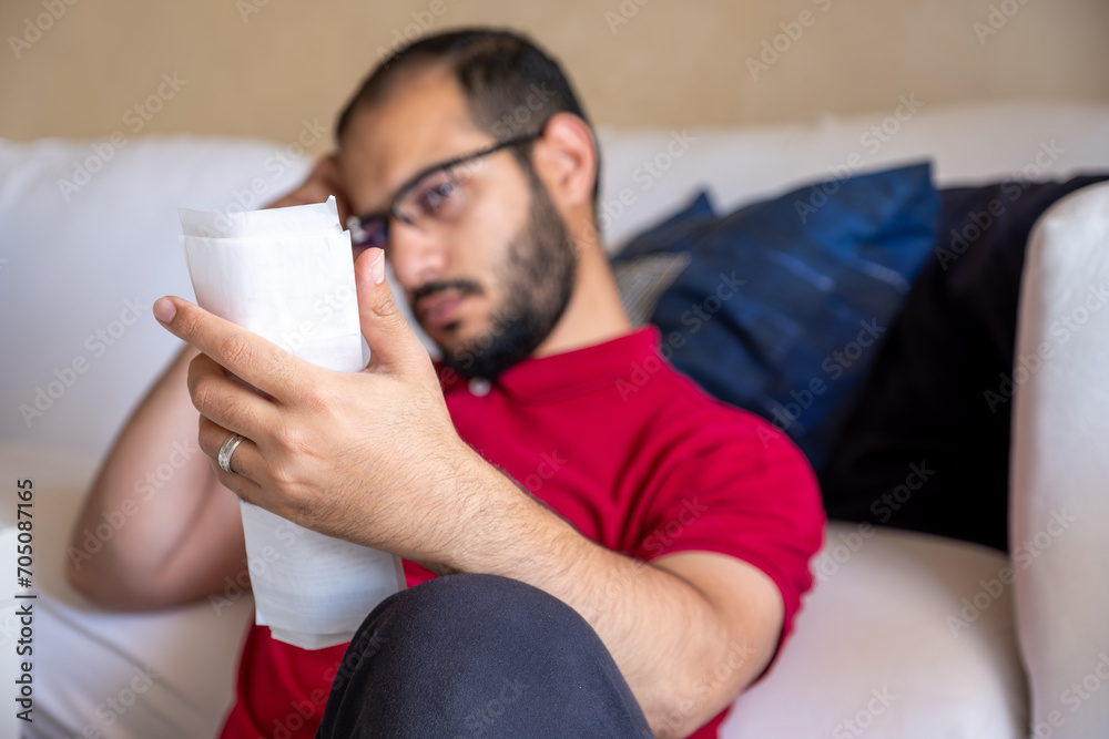man is frustrated from the living costs holding his bill and sitting in front of the couch man is frustrated from the living costs holding his bill and sitting in front of the couch