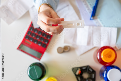 Female hands holding pregnancy tests with reciepts and callculator in the background to show the concept of prenancy costs