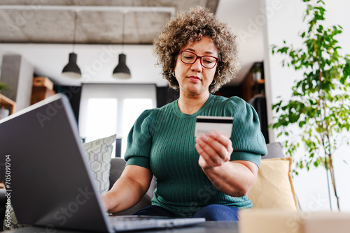 A cheerful mature woman is making an online purchase or payment, utilizing a credit card and a laptop computer. Online banking concept photo