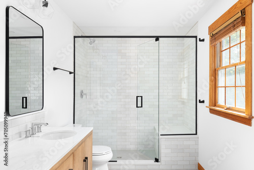 A beautiful luxury, modern bathroom with a light wood cabinet, walk-in shower with marble subway tiled walls, and black faucets and hardware. photo