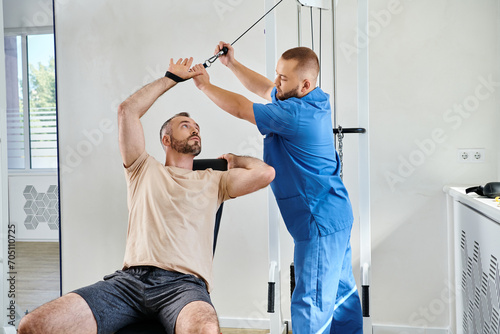 doctor in blue uniform helping man with recovery training on exercise machine in kinesio center