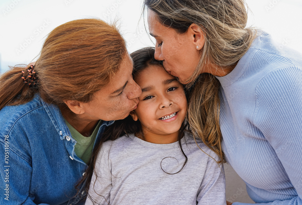 Latin multi generational family having tender moment outdoor - Female child smiling on camera while mother and grandmother kissing her face Latin multi generational family having tender moment outdoor - Female child smiling on camera while mother and grandmother kissing her face