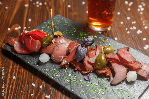 dried meat delicacy, basturma cut into pieces with cappers, on a slate board, beer glass, dark and moody, top new photo