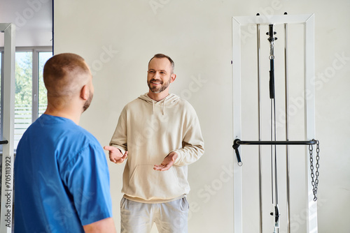 positive man talking to doctor in blue uniform during appointment in rehabilitation kinesio center