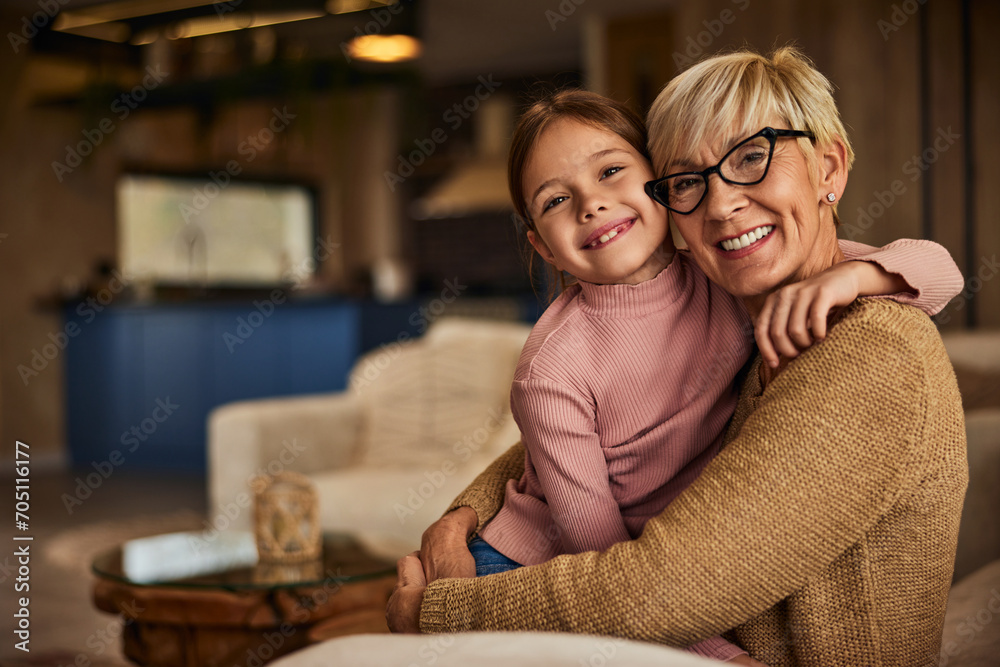 Portrait of a grandchild and her grandma smiling for the camera while sitting on the couch in the living room. Portrait of a grandchild and her grandma smiling for the camera while sitting on the couch in the living room.