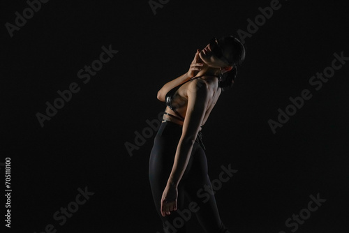 Young woman in black bodice and tights poses on black backlit studio background. Female dancer demonstrates elements of dance on high heels. Dance promo video concept.
