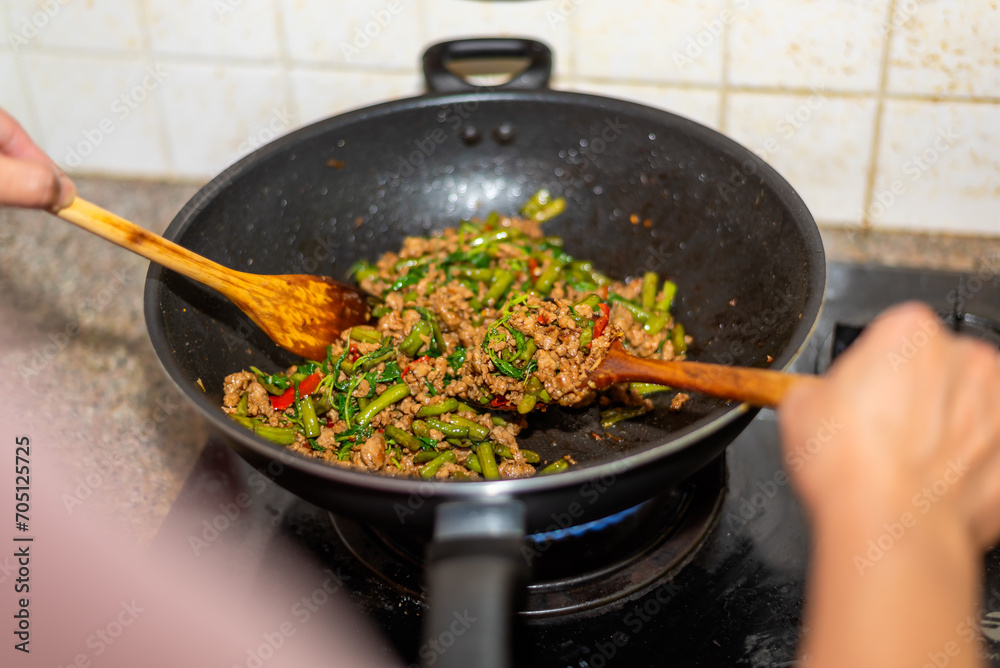 Woman cooking stir-fried pork with basil in real life home kitchen, Thai style food. Selective focus image. Woman cooking stir-fried pork with basil in real life home kitchen, Thai style food. Selective focus image.