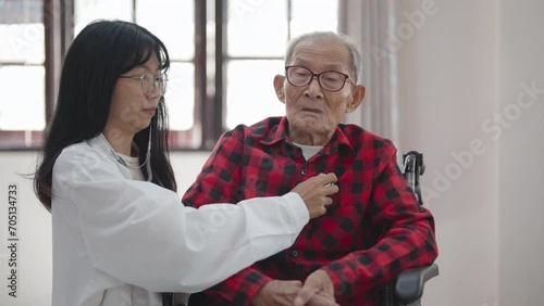 Asian Female doctor holding stethoscope examining old senior 60s grandpa patient in home healthcare concept. 