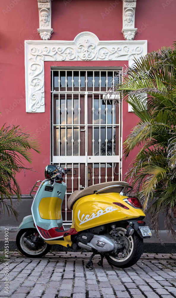 Vespa moped parked in front of a colorful colonial building window in