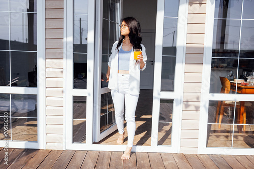 Young cute Asian woman opens glass door and goes out onto veranda of house.