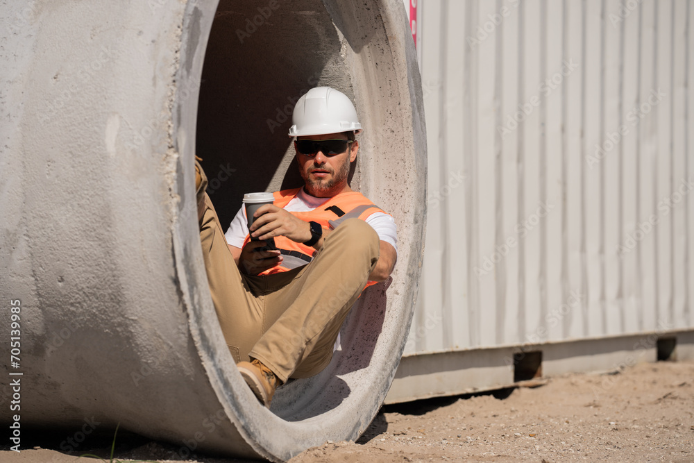 Coffee, engineer and construction worker relax on break at construction site. handsome male builder in hard hat smiling at camera. Construction Worker on Duty. Contractor and the Wooden House Frame Coffee, engineer and construction worker relax on break at construction site. handsome male builder in hard hat smiling at camera. Construction Worker on Duty. Contractor and the Wooden House Frame