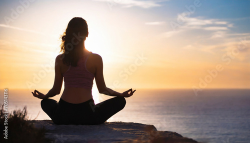 Young woman practicing yoga at sunset on a cliff overlooking the ocean.