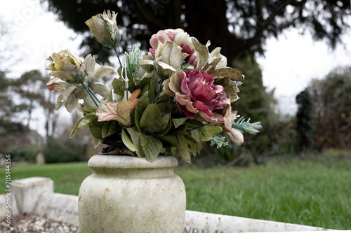 Shallow focus of fabric artificial flowers seen in a marge vase located on a large grave in a rural cemetery. The grave is located in a quite corner of the cemetery, near the church. photo