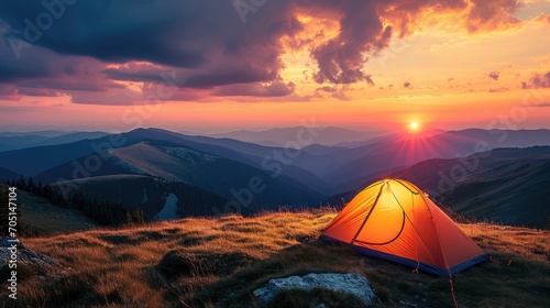 Glowing orange tent in the mountains under dramatic evening sky. Red sunset and mountains in the background. Summer landscape © buraratn