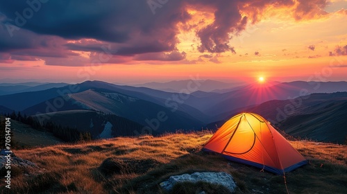 Glowing orange tent in the mountains under dramatic evening sky. Red sunset and mountains in the background. Summer landscape