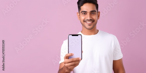 A youthful Indian gentleman dons a salmon-colored top and plain white tee, holding a mobile device with no display while giving a thumbs up against a pastel lavender backdrop.