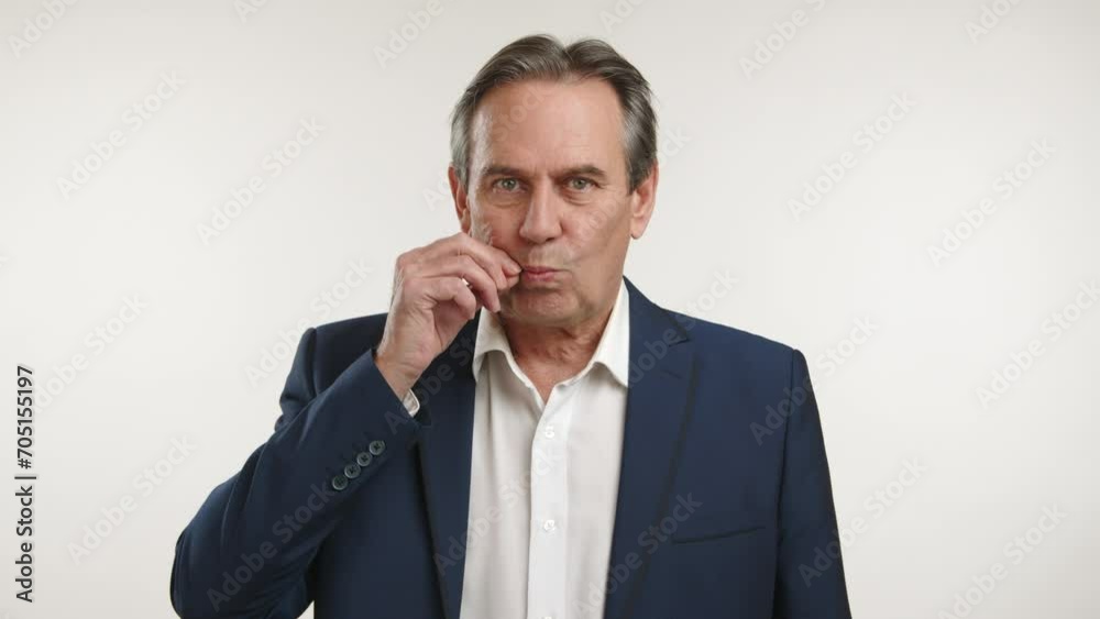 Distinguished man in a dark blue jacket and white shirt, making a hand gesture of locking lips, standing against a white background brightly lit. Camera 8K RAW. Distinguished man in a dark blue jacket and white shirt, making a hand gesture of locking lips, standing against a white background brightly lit. Camera 8K RAW.