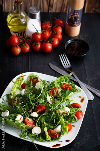 Fresh salad with cherry tomatoes, mozzarella cheese and arugula. wooden on a black background. 