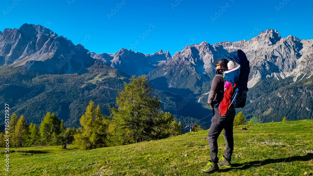 Hiker man with baby carrier with panoramic view of majestic mountain peaks of untamed Sexten Dolomites, South Tyrol, Italy, Europe. Hiking concept in Italian Alps. Looking at mount Dreischusterspitze